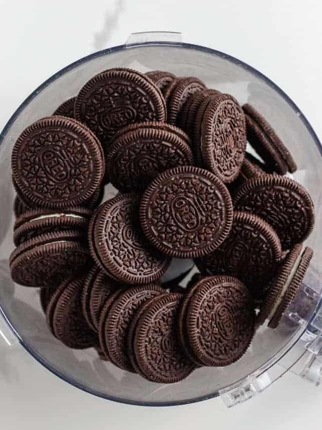 This Christmas dirt cake is a simple, no-bake dessert made with an Oreo crust, creamy whipped topping pudding layer and decorated with Little Debbie Christmas trees! Overhead view of whole Oreo cookies inside a food processor, ready to be crushed for the dirt cake crust.