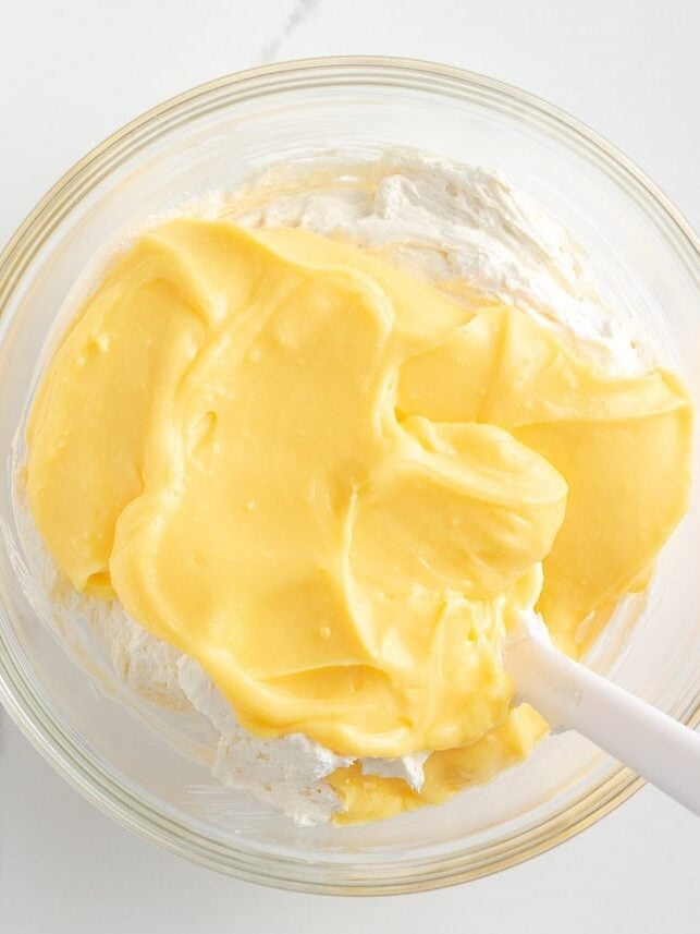 This Christmas dirt cake is a simple, no-bake dessert made with an Oreo crust, creamy whipped topping pudding layer and decorated with Little Debbie Christmas trees! Bowl of creamy vanilla pudding being folded into whipped cream cheese mixture with a spatula.