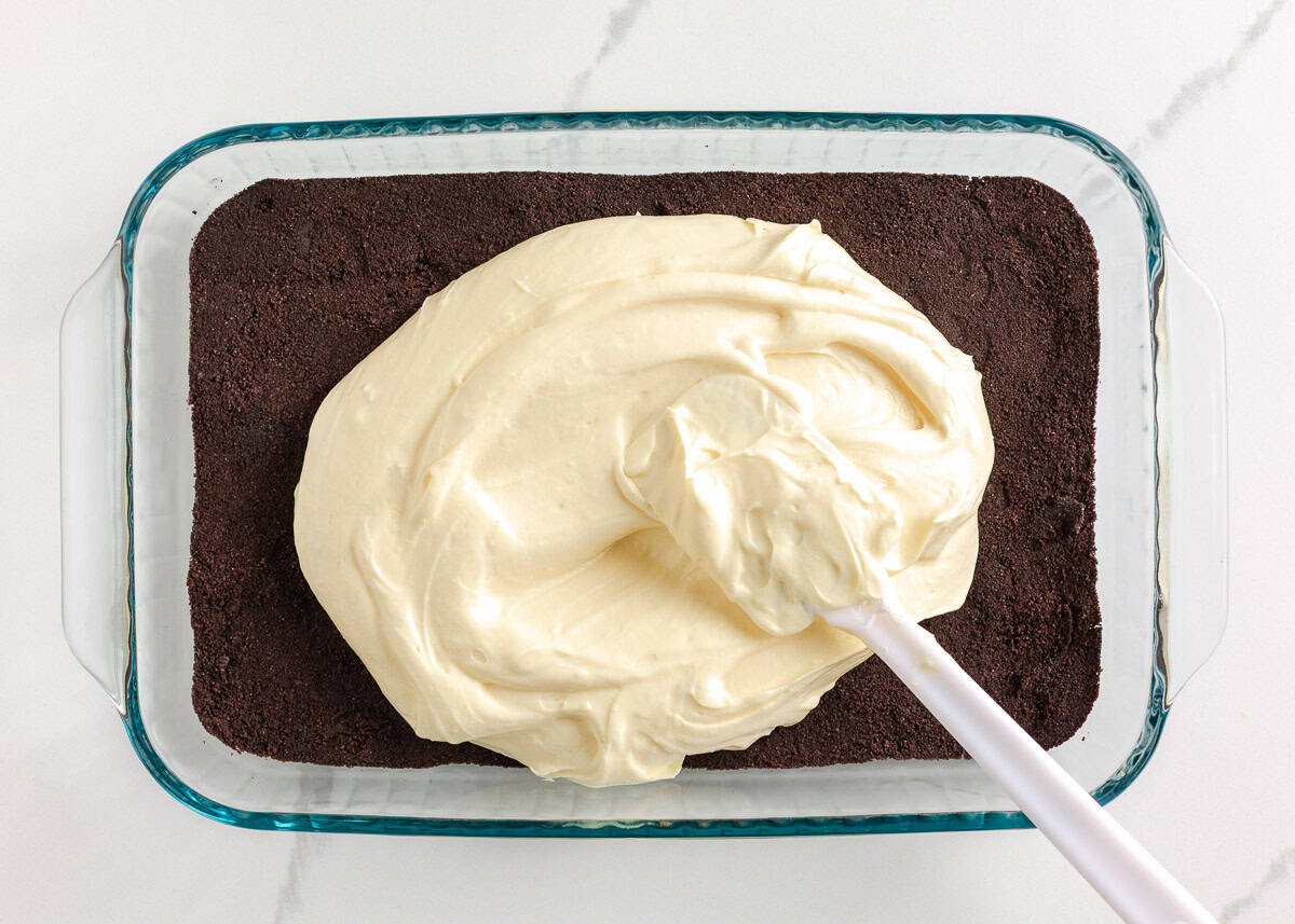 This Christmas dirt cake is a simple, no-bake dessert made with an Oreo crust, creamy whipped topping pudding layer and decorated with Little Debbie Christmas trees! Thick vanilla pudding filling spread over the Oreo crust in a baking dish with a spatula.