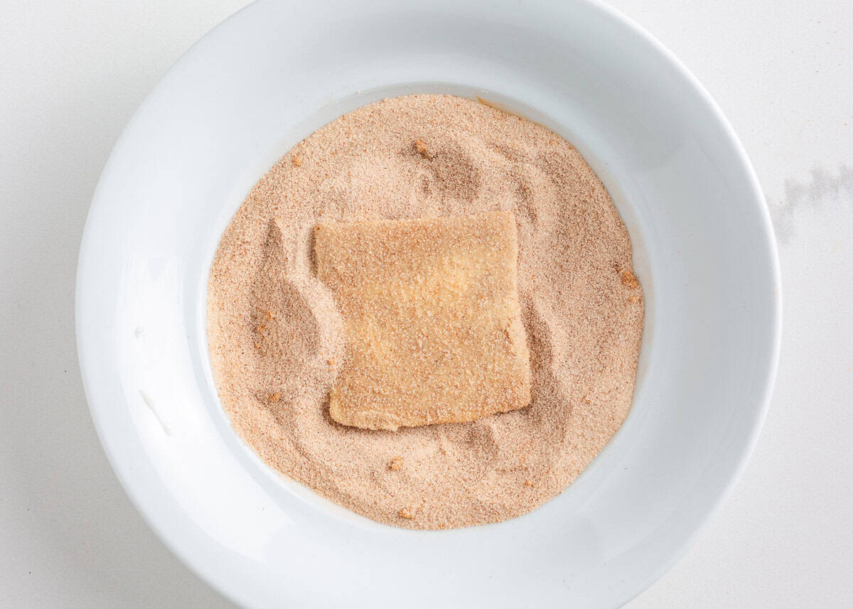 Bring home a taste of Disneyland with this churro toffee recipe. Buttery toffee coated in white chocolate and dusted with cinnamon sugar has classic churro flavor in every bite. Coated churro toffee square set into a bowl of cinnamon sugar for coating.