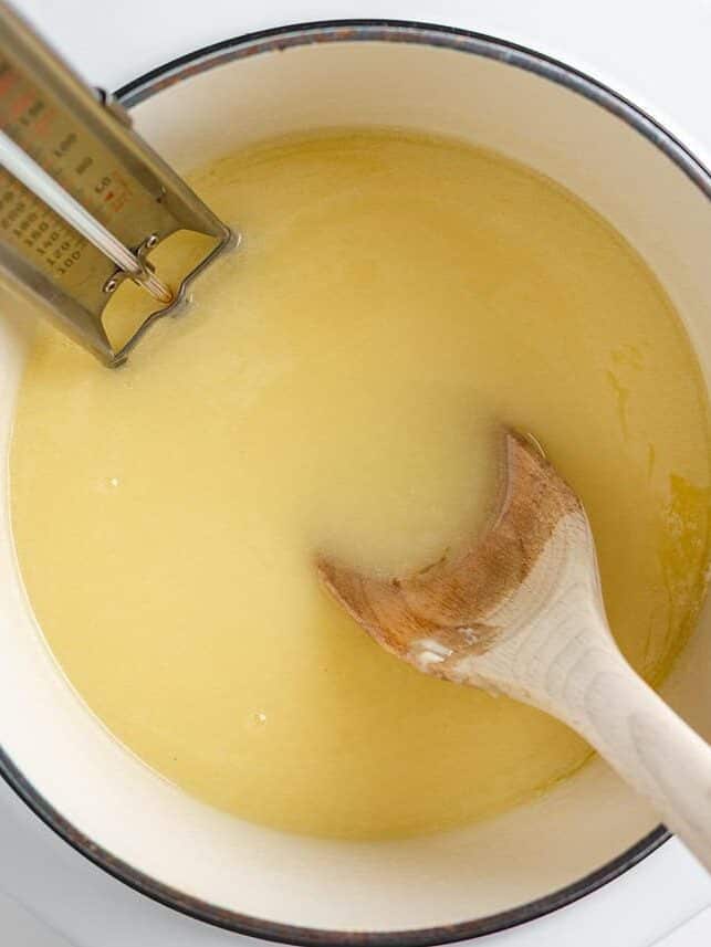 Bring home a taste of Disneyland with this churro toffee recipe. Buttery toffee coated in white chocolate and dusted with cinnamon sugar has classic churro flavor in every bite. Butter, sugar, and water mixture beginning to melt in a pot with a wooden spoon and candy thermometer.