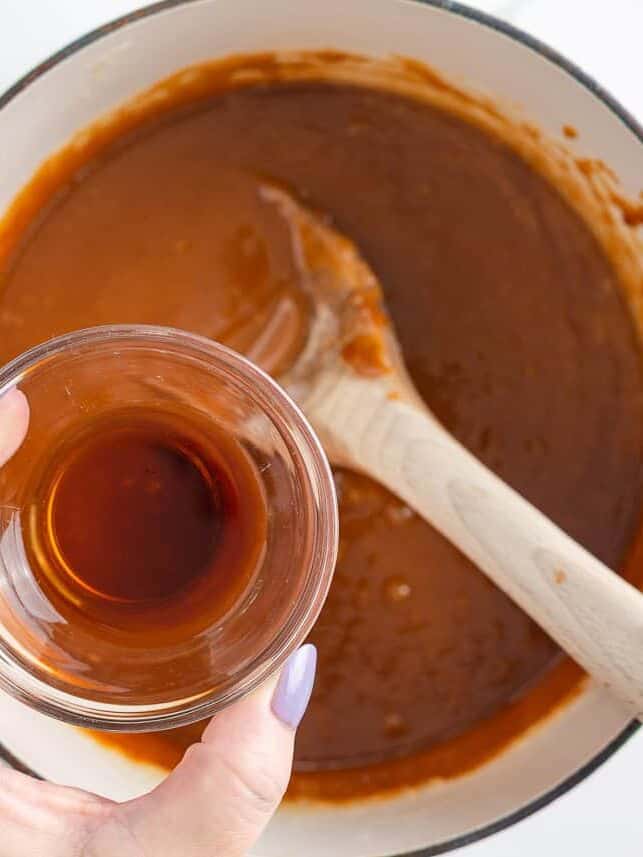 Bring home a taste of Disneyland with this churro toffee recipe. Buttery toffee coated in white chocolate and dusted with cinnamon sugar has classic churro flavor in every bite. Vanilla extract being poured into a pot of freshly cooked caramel while stirring with a wooden spoon.