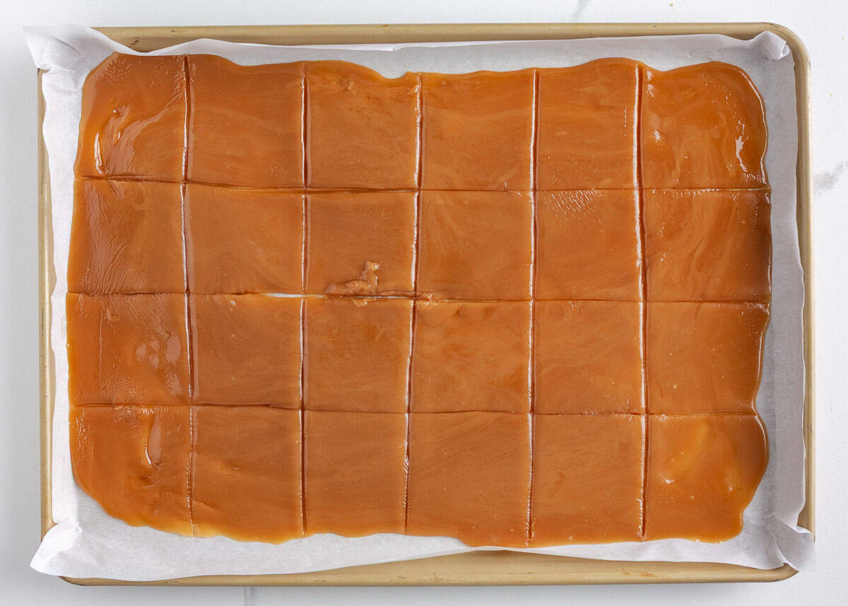 Bring home a taste of Disneyland with this churro toffee recipe. Buttery toffee coated in white chocolate and dusted with cinnamon sugar has classic churro flavor in every bite. Sheet of sliced churro toffee cooling on a parchment-lined baking sheet before dipping.