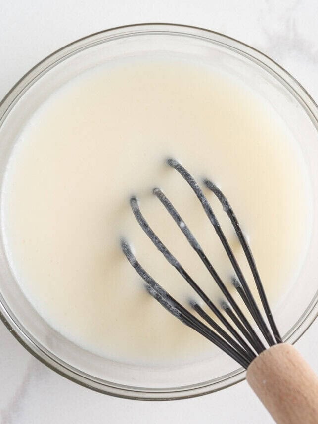 Originally inspired by The Gilmore Girls, these coffee cake cookies are made with a soft and chewy cinnamon-infused brown sugar cookie with a crumb topping and vanilla glaze! Simple powdered sugar glaze being whisked in a glass bowl for coffee cake cookies.