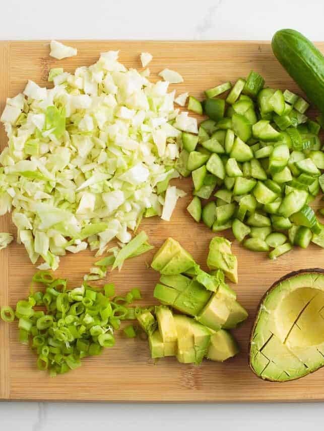 Learn to make this TikTok Green Goddess Salad with the best, most flavorful homemade green goddess salad dressing you're going to want to put on everything! Chopped cabbage, cucumbers, avocado, and sliced green onions on a cutting board for green goddess salad.