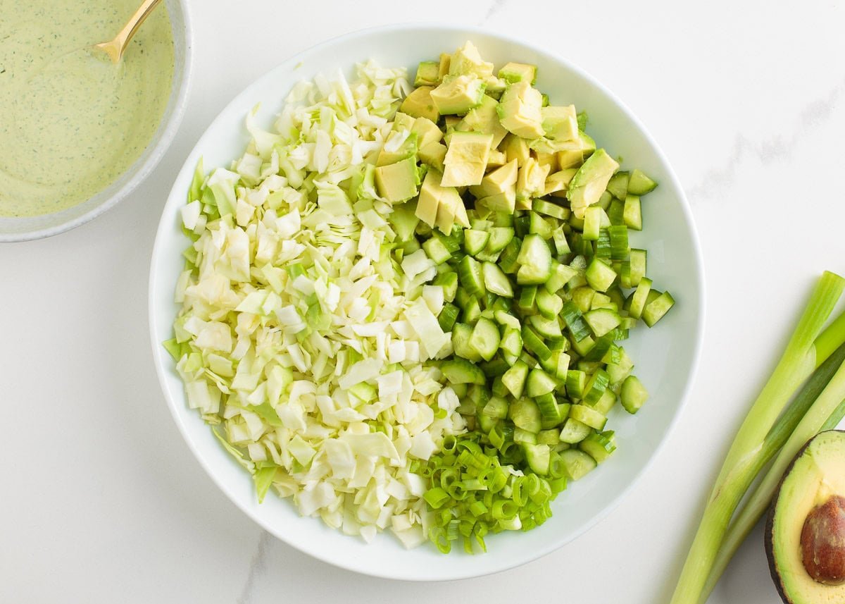 Learn to make this TikTok Green Goddess Salad with the best, most flavorful homemade green goddess salad dressing you're going to want to put on everything! Chopped cabbage, cucumbers, avocado, and green onions arranged in a bowl before adding green goddess dressing.
