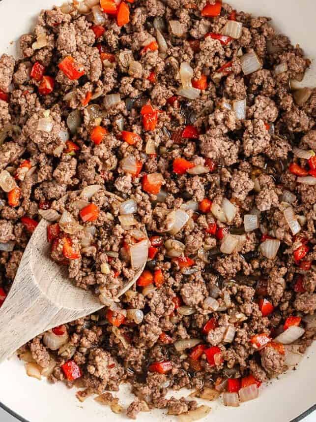 Asian-inspired ground beef lettuce wraps are easy, satisfying, and better than takeout with a juicy, sweet and spicy filling wrapped in crisp butter leaves and ready in 15 minutes. Cooked ground beef mixture with onions, red bell peppers, garlic, and ginger in a large skillet with a wooden spoon.