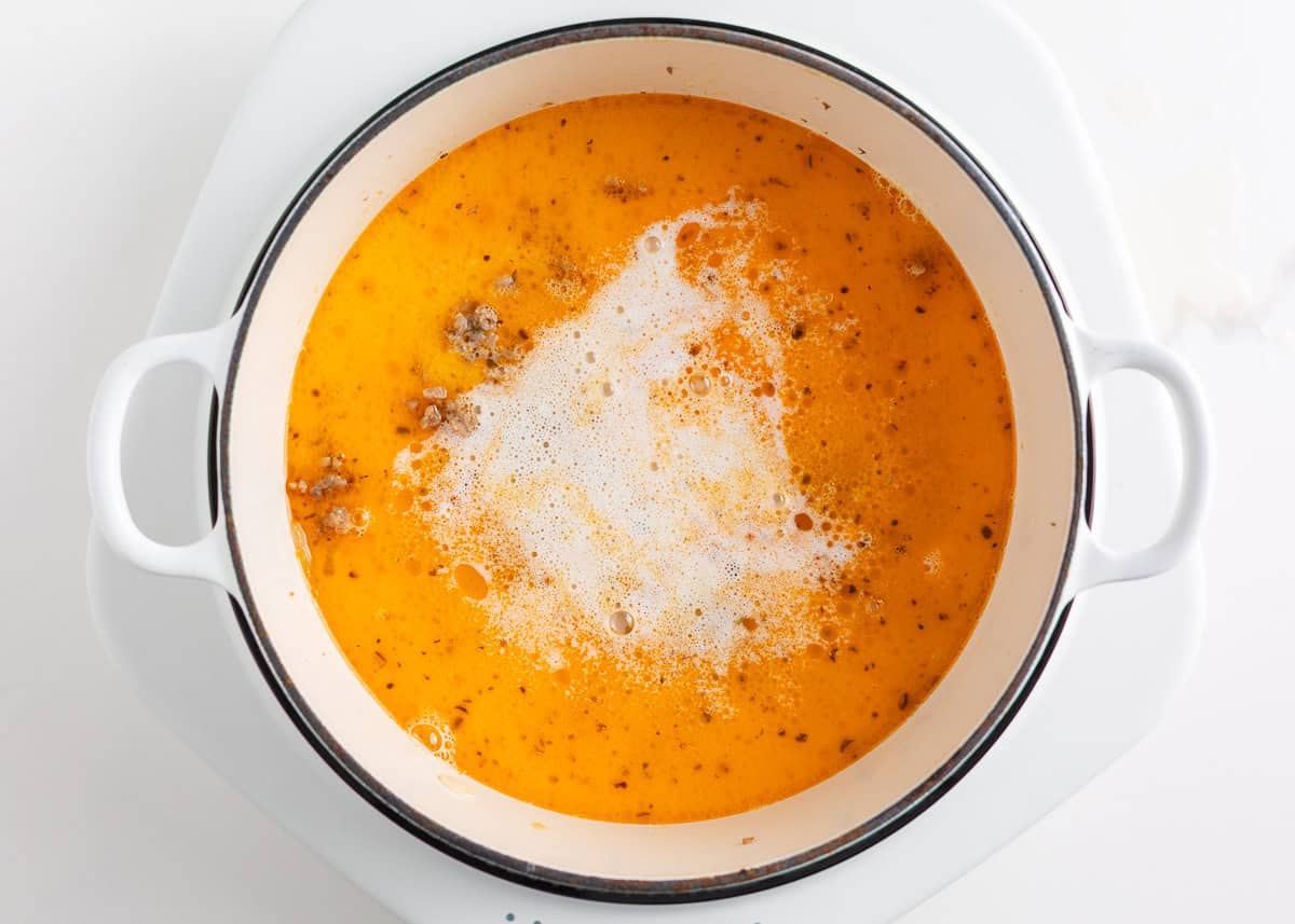 This orecchiette pasta with sausage and broccoli is simmered in a light, creamy sauce until the pasta is tender and the broccoli is bright. It’s a comforting one-pan meal ready in 30 minutes! A pot filled with chicken broth and cream simmering with small pieces of cooked sausage before the pasta is added.