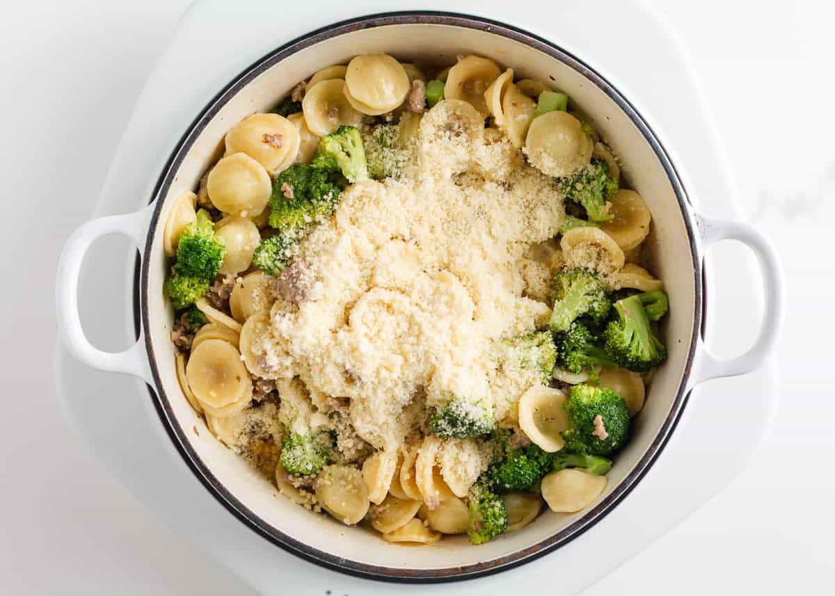 This orecchiette pasta with sausage and broccoli is simmered in a light, creamy sauce until the pasta is tender and the broccoli is bright. It’s a comforting one-pan meal ready in 30 minutes! Cooked orecchiette and broccoli in a pot covered with a large mound of grated Parmesan cheese before stirring.