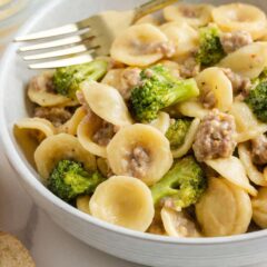 A bowl of orecchiette pasta coated in a creamy sauce with pieces of sausage and broccoli, served with slices of bread on the side.