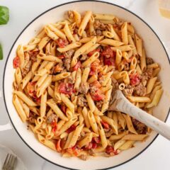 Creamy Italian sausage pasta in a white skillet with penne noodles, cooked sausage, and tomatoes mixed together.