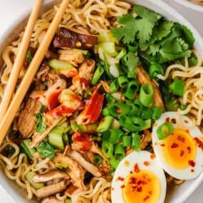 Overhead view of homemade chicken ramen topped with shredded chicken, bok choy, green onions, mushrooms, and soft-boiled eggs.