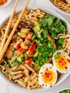 Overhead view of homemade chicken ramen topped with shredded chicken, bok choy, green onions, mushrooms, and soft-boiled eggs.