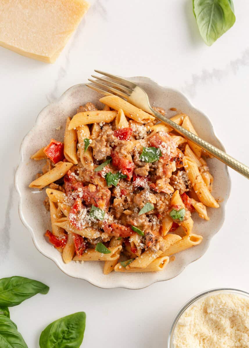 A creamy, zesty pasta recipe is something everyone needs for busy days and cozy weekends. Italian sausage pasta is a family favorite and easy to make in 30 minutes! Plate of creamy Italian sausage penne pasta topped with grated parmesan and fresh basil.
