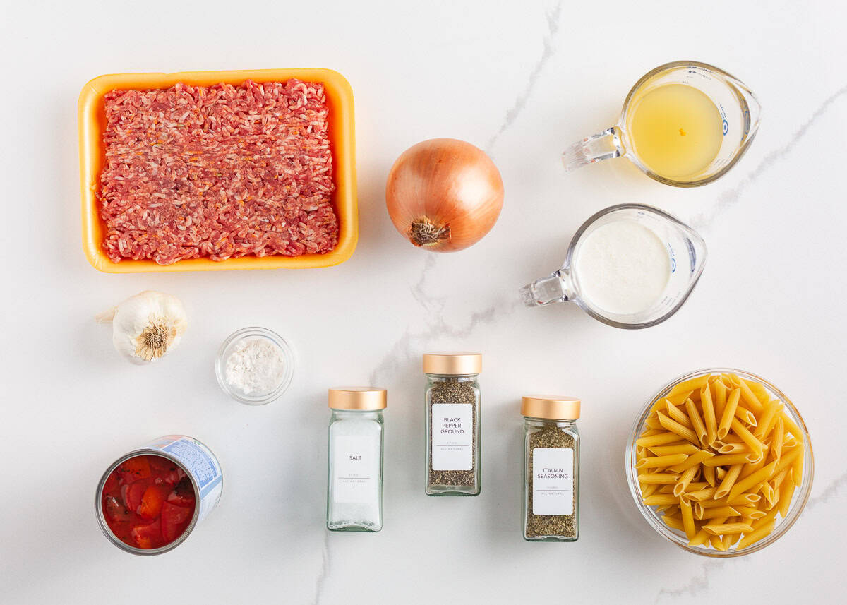 A creamy, zesty pasta recipe is something everyone needs for busy days and cozy weekends. Italian sausage pasta is a family favorite and easy to make in 30 minute Ingredients for creamy Italian sausage pasta arranged on a white surface, including Italian sausage, onion, garlic, penne pasta, canned tomatoes, broth, cream, flour, salt, pepper, and Italian seasoning.