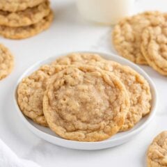Soft and chewy oatmeal cookies stacked on a small white plate with more cookies in the background.