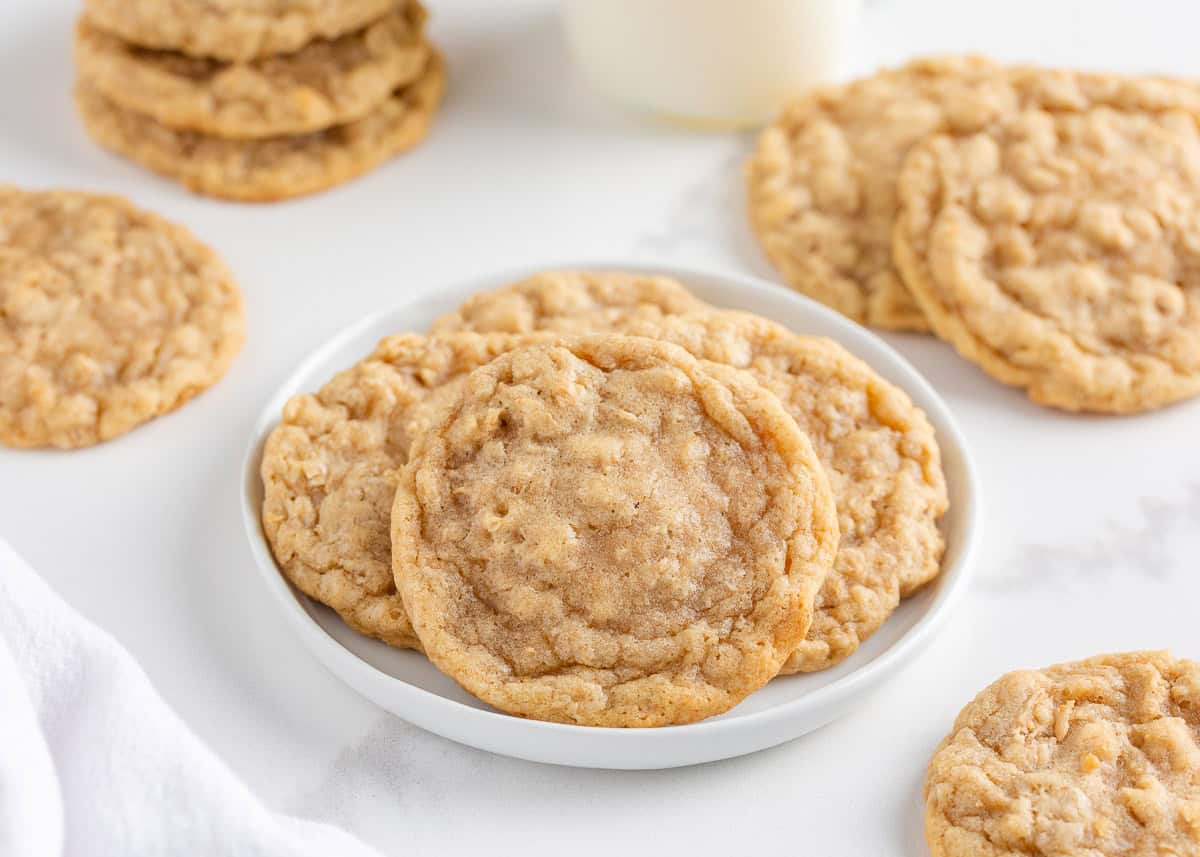These easy oatmeal cookies are a quick treat made in only one bowl. They turn perfectly every time with a buttery brown sugar taste, crisp edges and a soft, chewy center! Soft and chewy oatmeal cookies stacked on a small white plate with more cookies in the background.