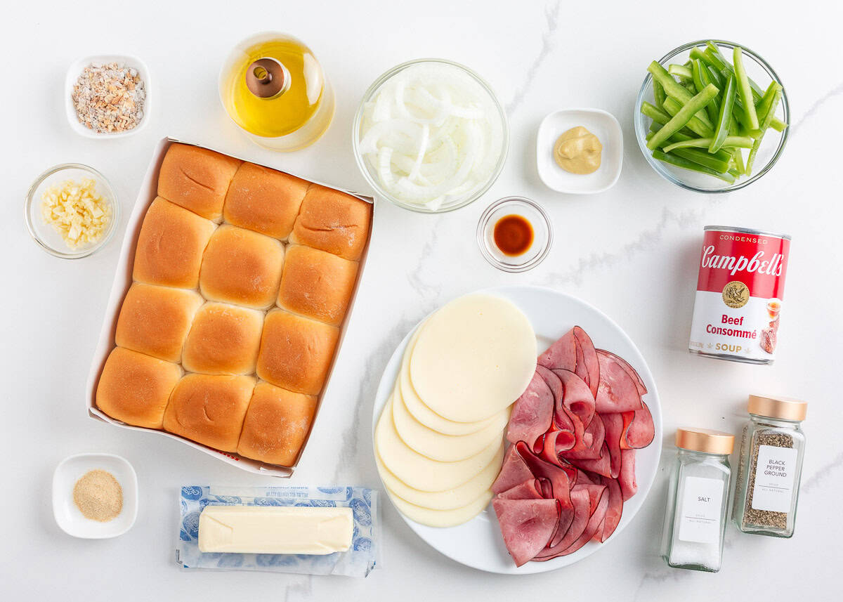 Philly cheesesteak sliders made with Hawaiian rolls stuffed with roast beef, sautéed peppers and onions, and melty cheese. A crowd-pleasing mini version of the classic! Overhead view of ingredients for Philly cheesesteak sliders including Hawaiian rolls, roast beef, provolone, sautéed onions and peppers, butter, spices, and beef consommé.