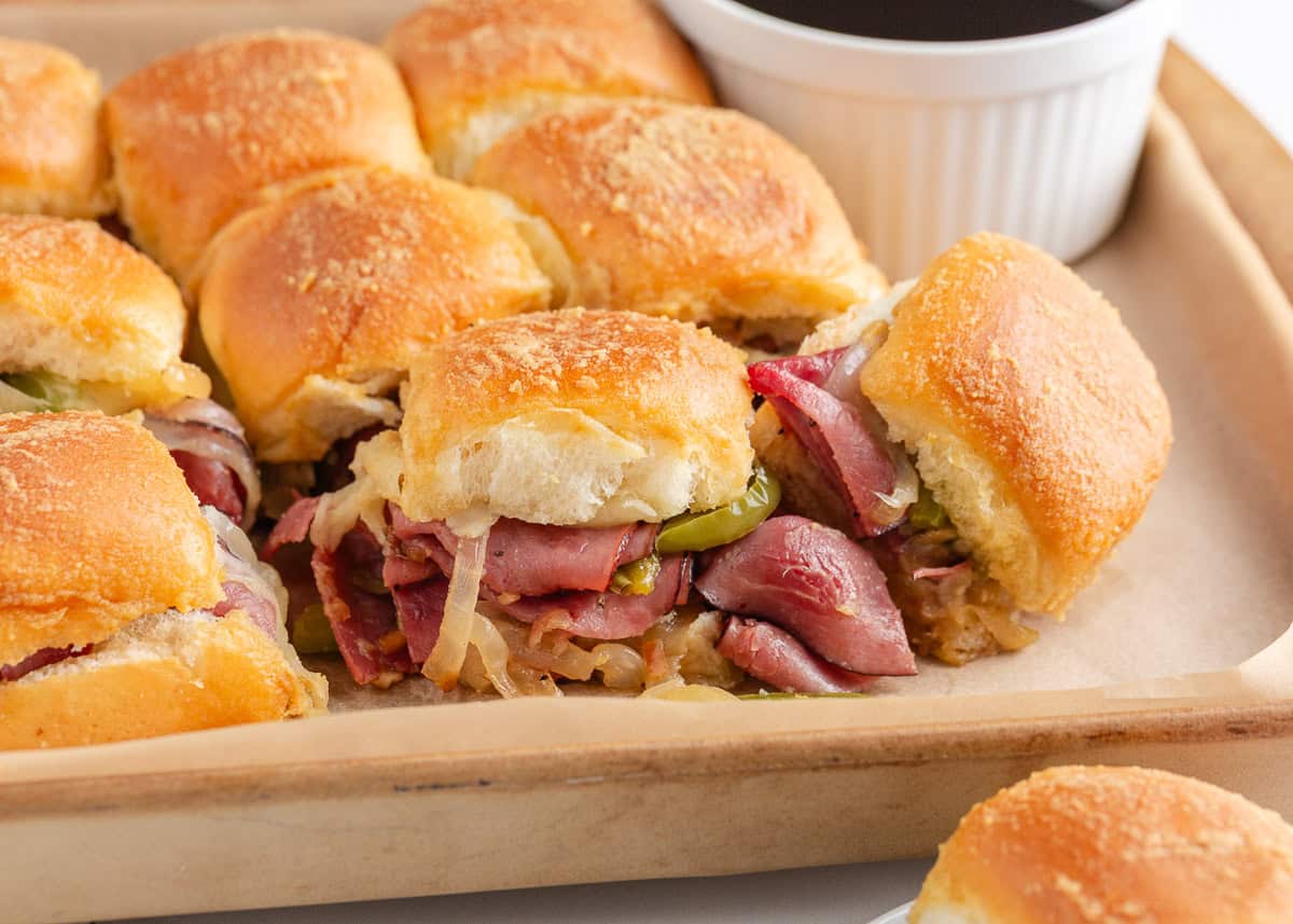 Close-up of a Philly cheesesteak slider showing tender roast beef, peppers, onions, and melted cheese inside soft toasted rolls.