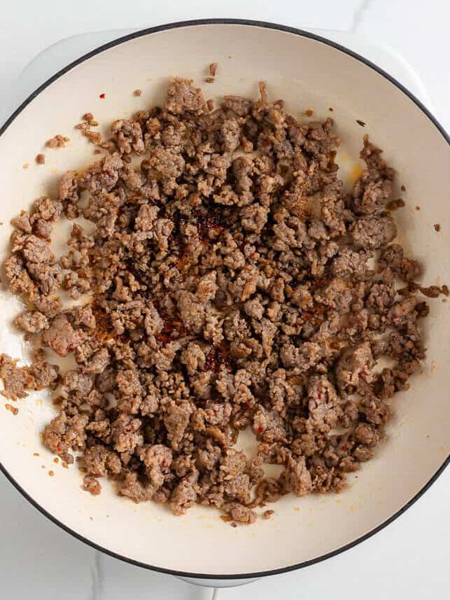 A creamy, zesty pasta recipe is something everyone needs for busy days and cozy weekends. Italian sausage pasta is a family favorite and easy to make in 30 minutes! Italian sausage crumbled and browned in a white skillet.