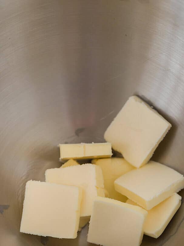 Cold cubes of butter sitting at the bottom of a metal mixing bowl before creaming.