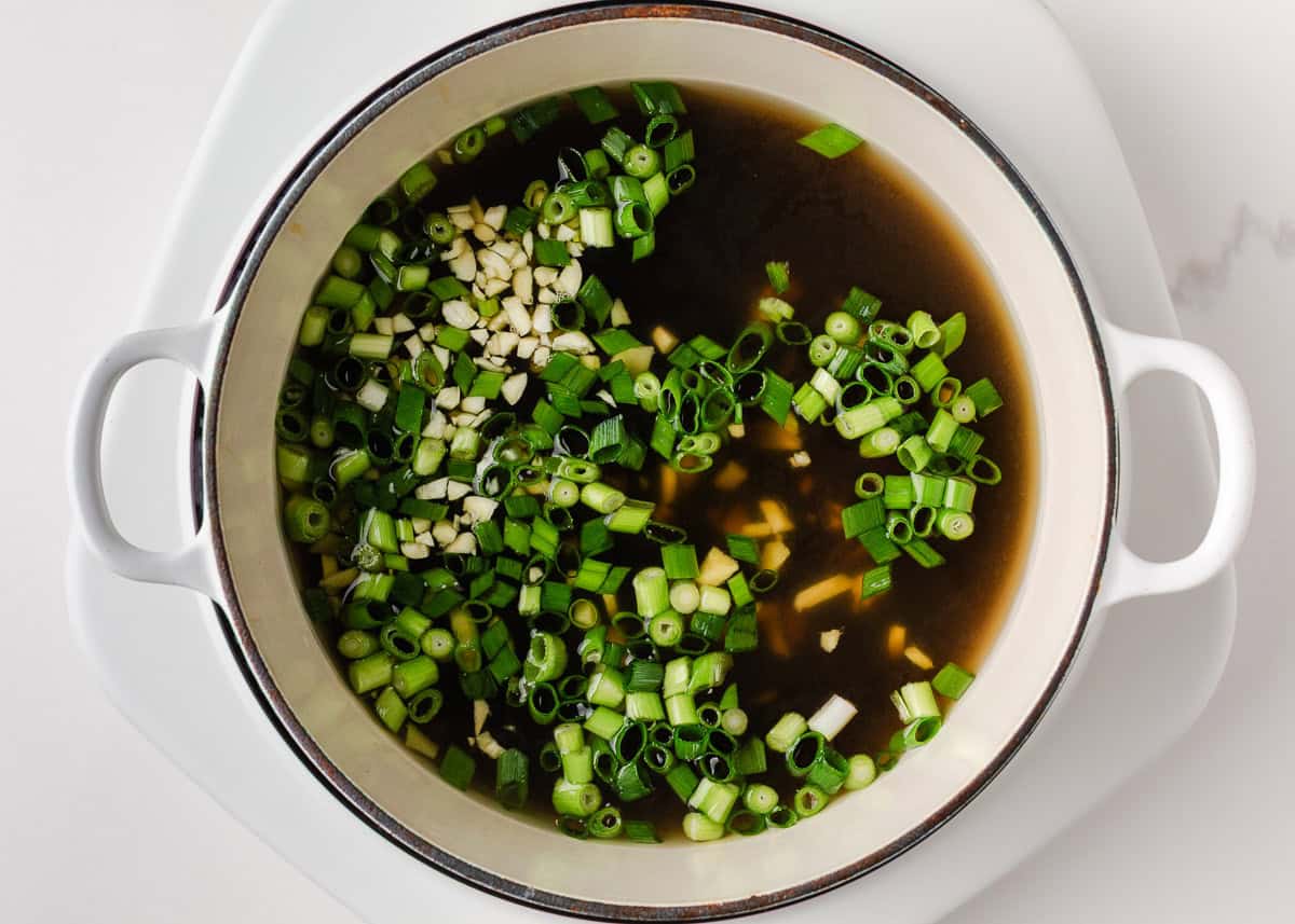 Make this quick and easy homemade chicken ramen with a rich savory broth, tender chicken, noodles, and plenty of your favorite toppings. Chicken broth simmering with green onions, garlic, and ginger in a large pot.