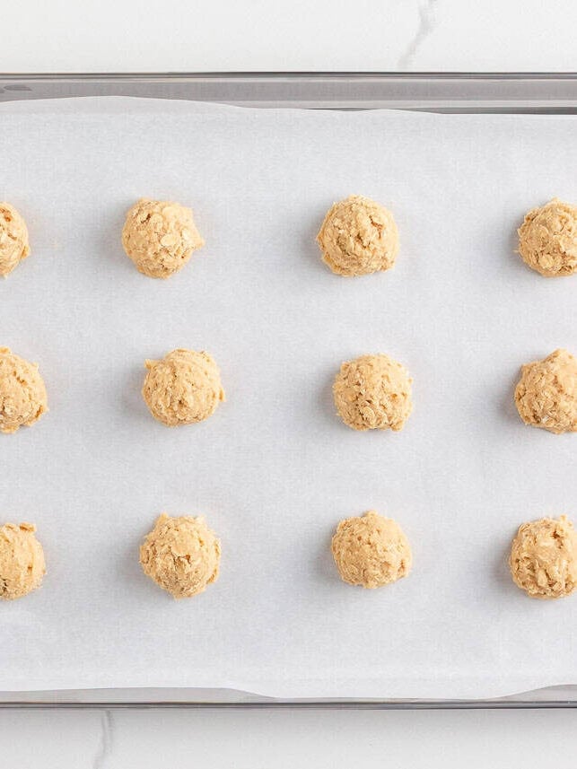 Scoops of oatmeal cookie dough spaced evenly on a parchment-lined baking sheet before baking.
