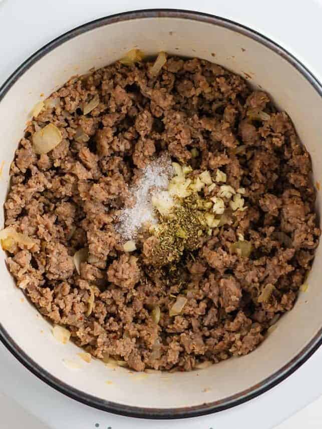 This orecchiette pasta with sausage and broccoli is simmered in a light, creamy sauce until the pasta is tender and the broccoli is bright. It’s a comforting one-pan meal ready in 30 minutes! Browned sausage and onions in a pot with minced garlic, Italian seasoning, and salt added on top.