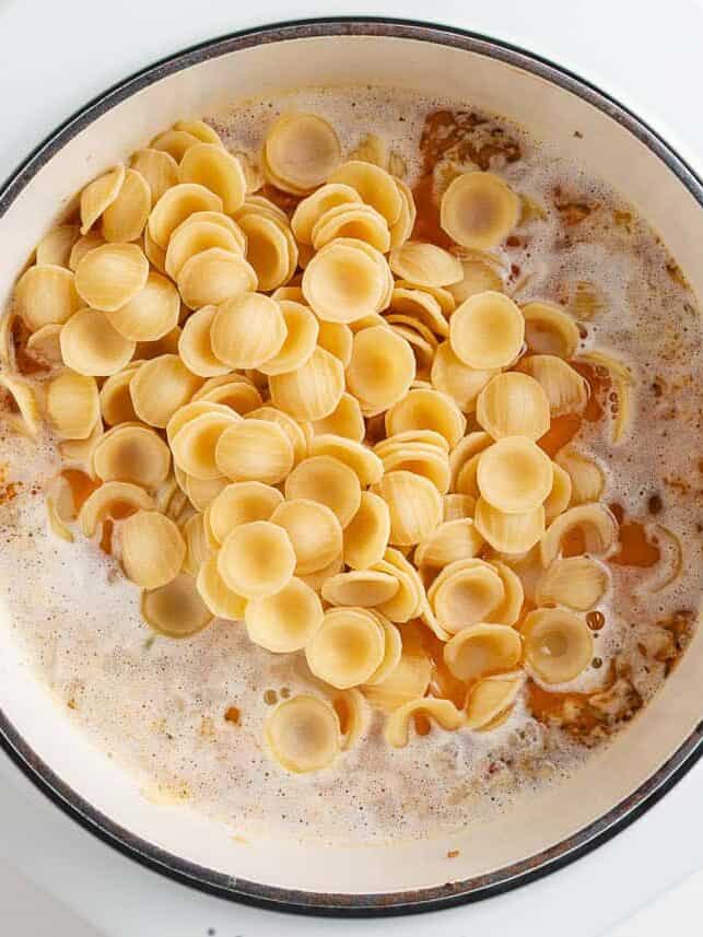 This orecchiette pasta with sausage and broccoli is simmered in a light, creamy sauce until the pasta is tender and the broccoli is bright. It’s a comforting one-pan meal ready in 30 minutes! Dry orecchiette pasta poured into a pot of simmering broth and browned sausage.