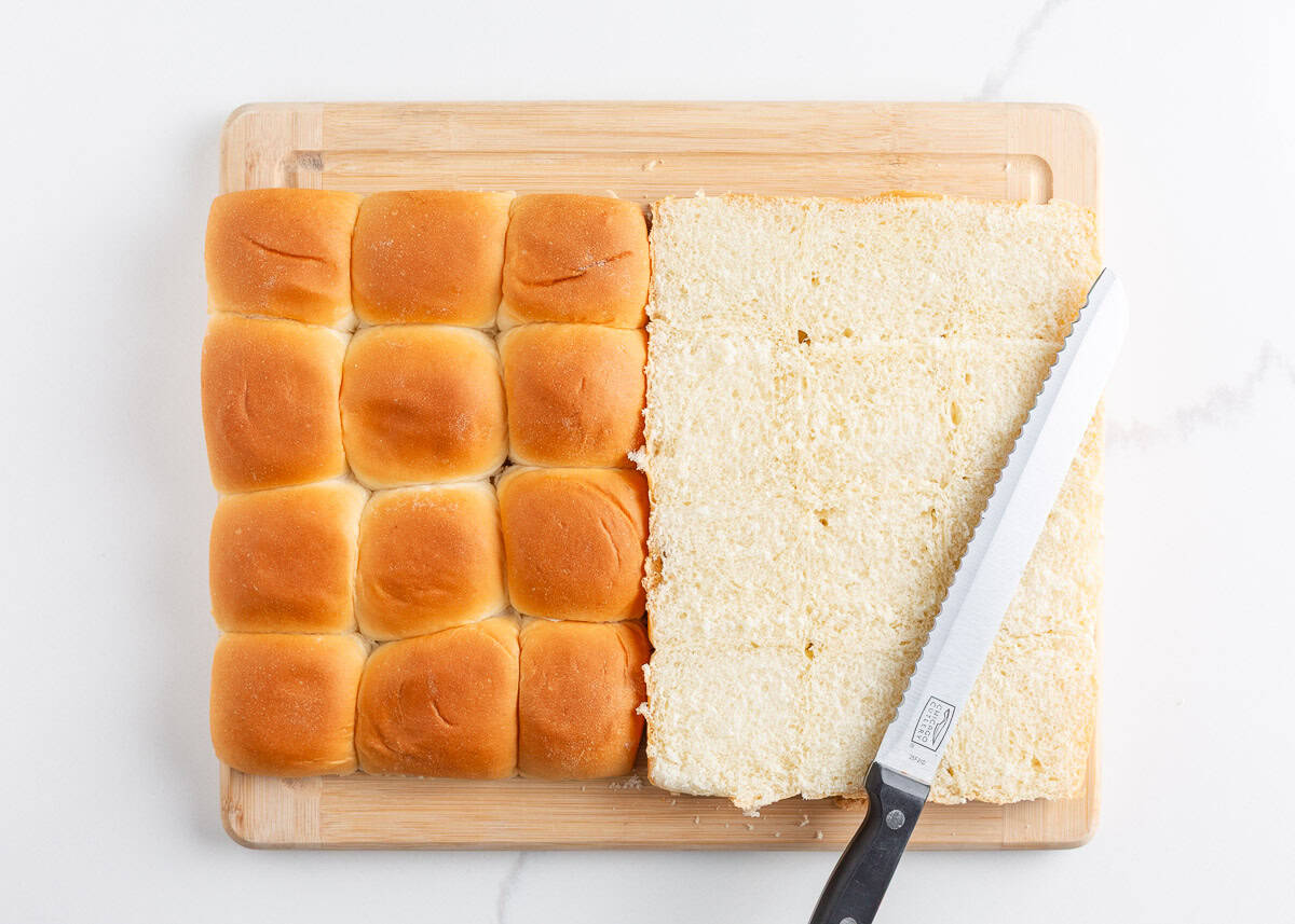 Philly cheesesteak sliders made with Hawaiian rolls stuffed with roast beef, sautéed peppers and onions, and melty cheese. A crowd-pleasing mini version of the classic! Whole sheet of Hawaiian rolls sliced horizontally on a cutting board with a serrated knife.