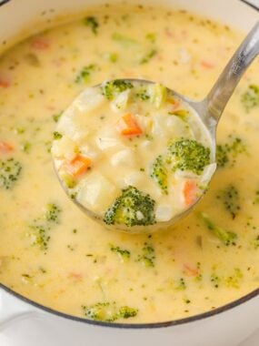 Ladle of creamy broccoli cheese and potato soup with tender potatoes, carrots, and broccoli.