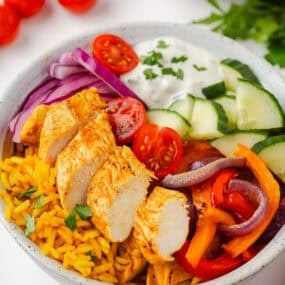Chicken shawarma bowls with spiced chicken, yellow rice, cucumbers, tomatoes, and creamy sauce.