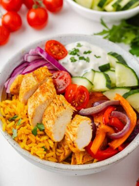 Chicken shawarma bowls with spiced chicken, yellow rice, cucumbers, tomatoes, and creamy sauce.