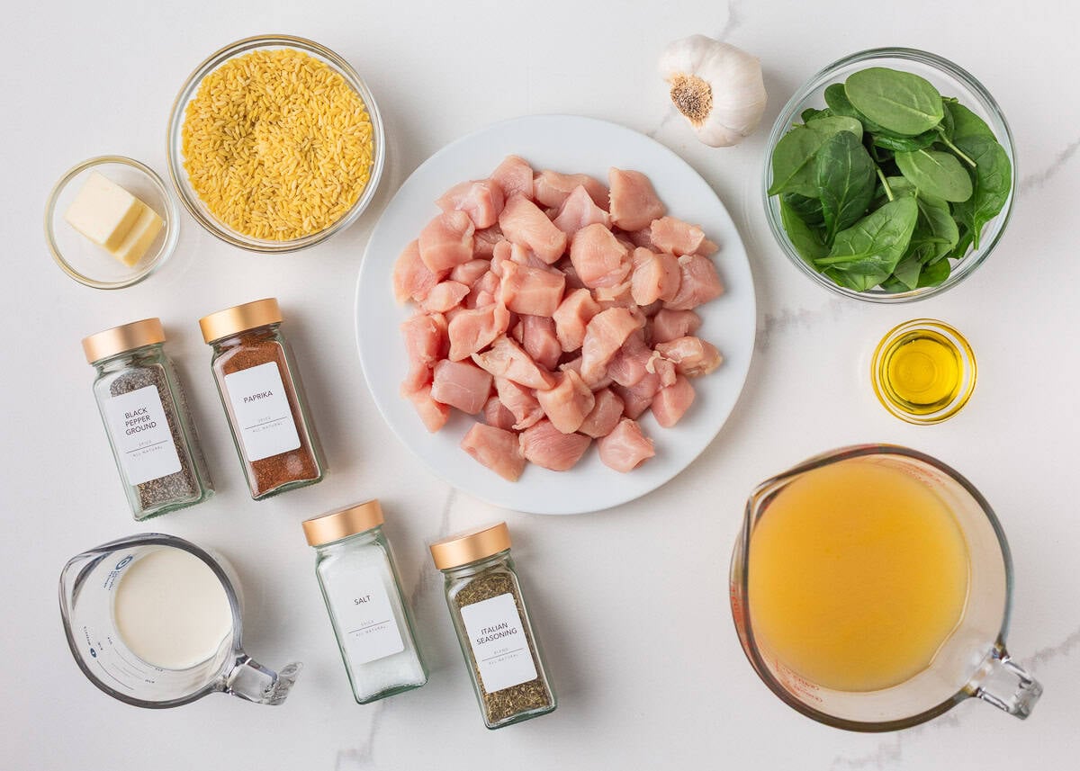 Ingredients for chicken and orzo including cubed chicken, uncooked orzo, spinach, chicken broth, cream, garlic, olive oil, and seasonings.