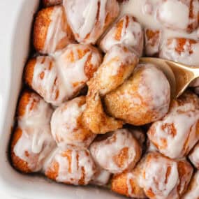 Gooey cinnamon roll bites with vanilla glaze being lifted from the baking dish.