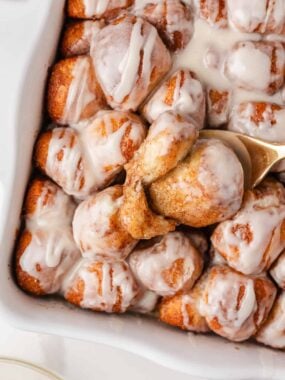 Gooey cinnamon roll bites with vanilla glaze being lifted from the baking dish.