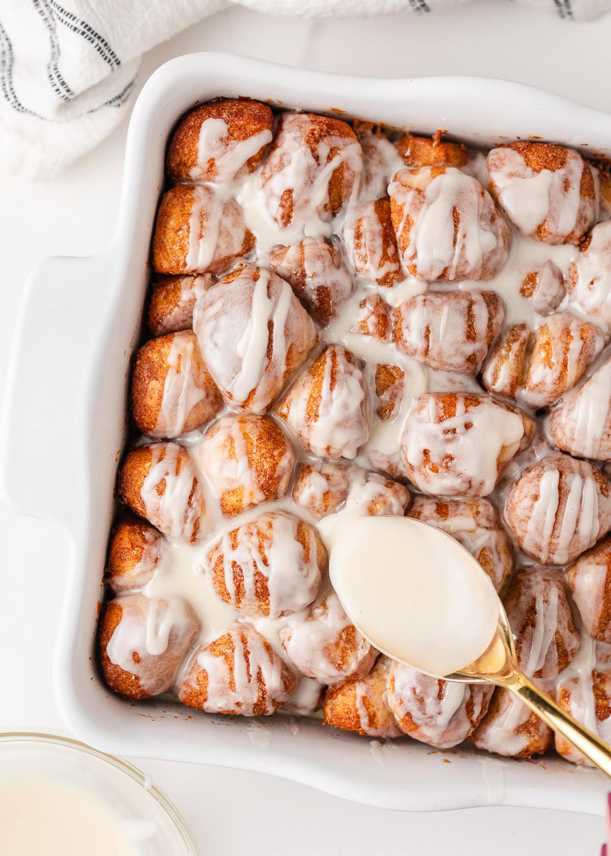 These easy cinnamon roll bites deliver soft, fluffy cinnamon sugar goodness in a bite-sized treat made with ready-made frozen dough. They're perfectly gooey for a sweet treat! Gooey cinnamon roll bites baked in a square dish with icing being drizzle over them.