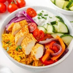 Close-up of chicken shawarma bowls with sliced chicken, roasted vegetables, fresh cucumber, cherry tomatoes and yogurt sauce.