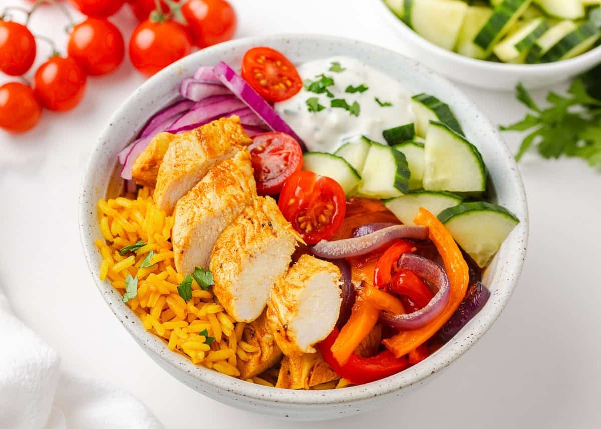 Close-up of chicken shawarma bowls with sliced chicken, roasted vegetables, fresh cucumber, cherry tomatoes and yogurt sauce.
