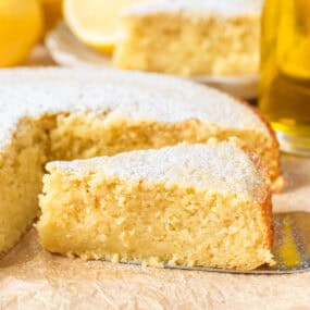 Lemon olive oil cake dusted with powdered sugar with one slice removed to show soft texture.