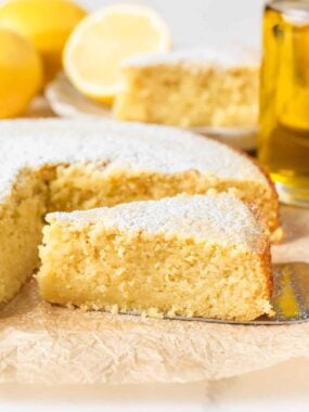 Lemon olive oil cake dusted with powdered sugar with one slice removed to show soft texture.