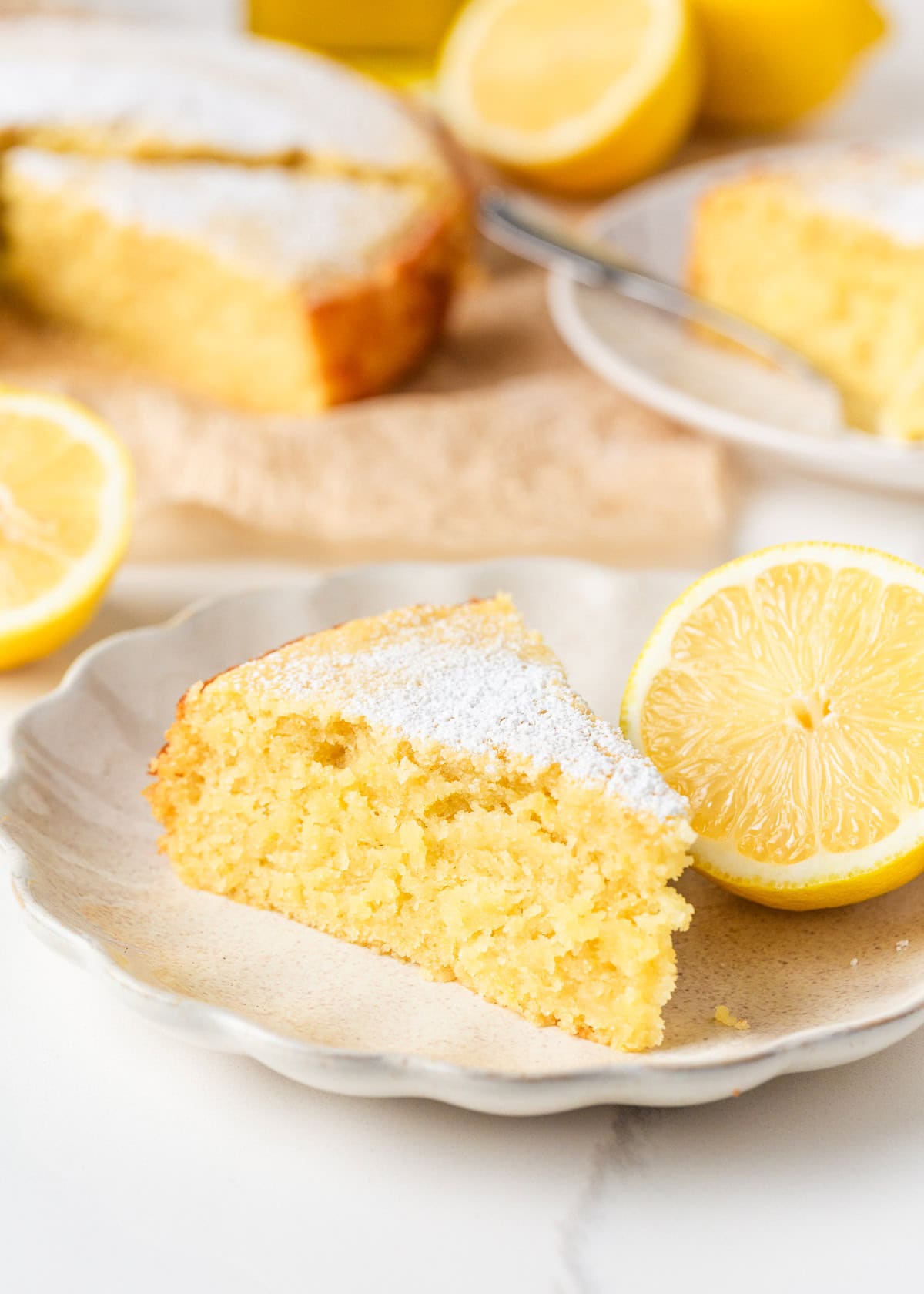 This lemon olive oil cake is sunshine in dessert form, with a light, tender crumb and bright lemon flavor in every bite. Elegant yet simple, it’s an effortless cake to make. Slice of lemon olive oil cake dusted with powdered sugar served on a plate with fresh lemon.