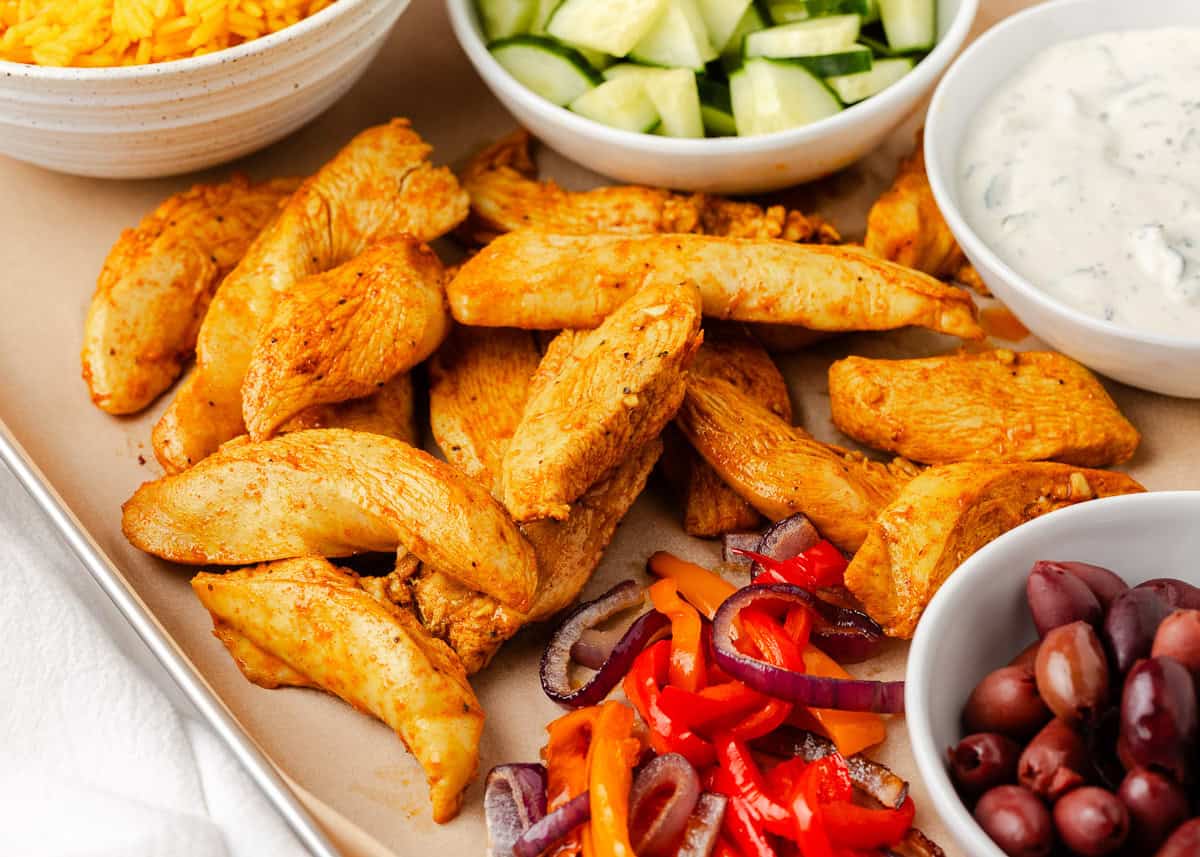 Colorful, fresh, and customizable, these chicken shawarma bowls are packed with bold spices, tender chicken, and all your favorite toppings. Close-up of roasted chicken and vegetables an a sheet pan for chicken shawarma bowls.