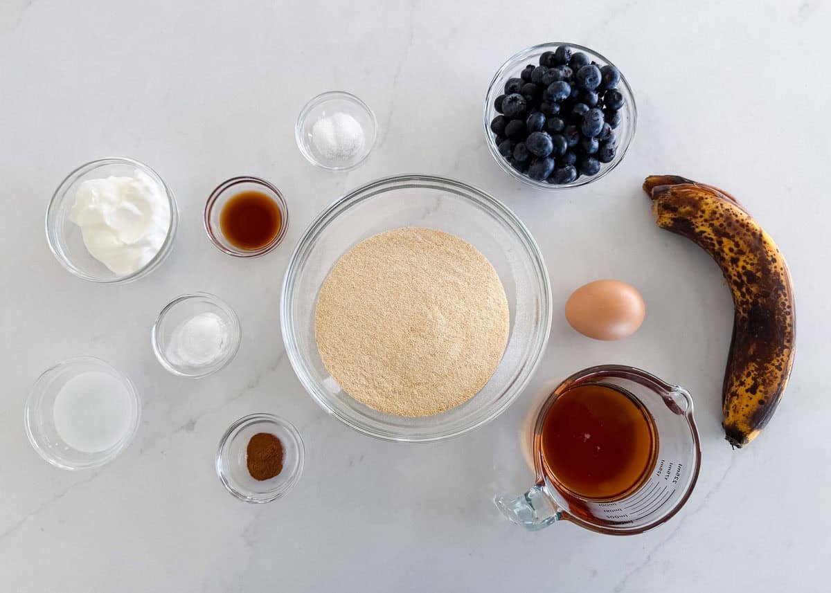 Bake up a moist and healthy blueberry banana bread in just over an hour using coconut oil, whole wheat flour, maple syrup, and loads of sweet bananas and juicy blueberries! Ingredients for blueberry banana bread including ripe banana, blueberries, flour, maple syrup, egg, sour cream, and cinnamon.