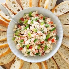 Feta dip made with crumbled feta cheese, chopped tomatoes, green onions, and cucumber served in a bowl with sliced crusty bread.