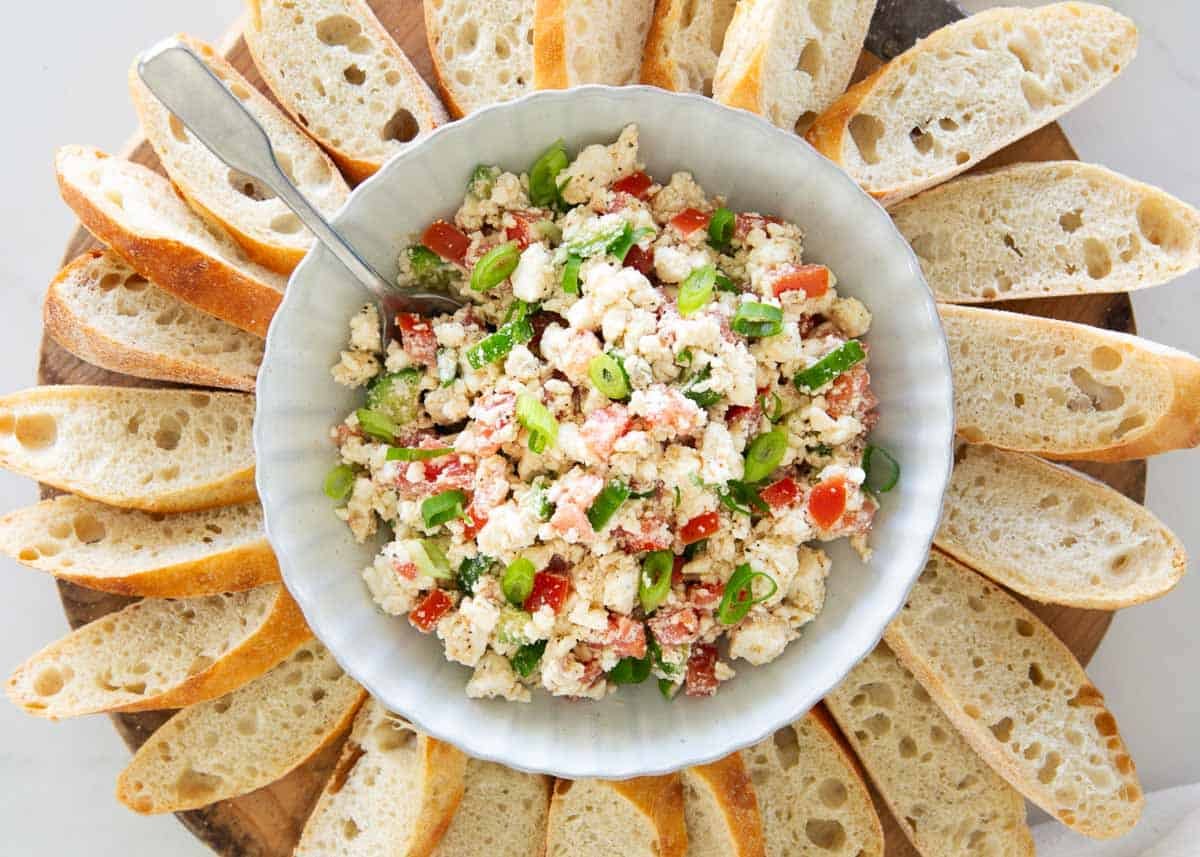 Feta dip made with crumbled feta cheese, chopped tomatoes, green onions, and cucumber served in a bowl with sliced crusty bread.