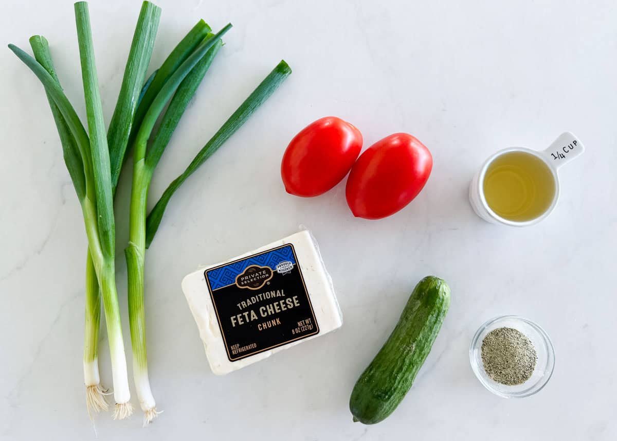 This feta dip comes together in 5 minutes with crumbled feta cheese, fresh vegetables, olive oil, and Greek seasoning. Serve it with crusty bread for an effortless appetizer. Ingredients for feta dip including block feta cheese, roma tomatoes, green onions, baby cucumber, olive oil, and Greek seasoning.