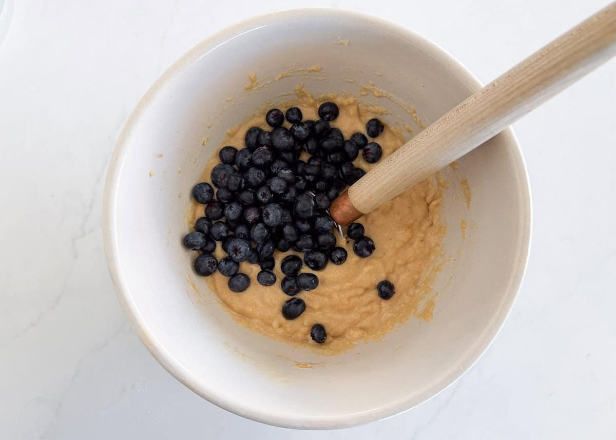 Bake up a moist and healthy blueberry banana bread in just over an hour using coconut oil, whole wheat flour, maple syrup, and loads of sweet bananas and juicy blueberries! Fresh blueberries being folded into banana bread batter.