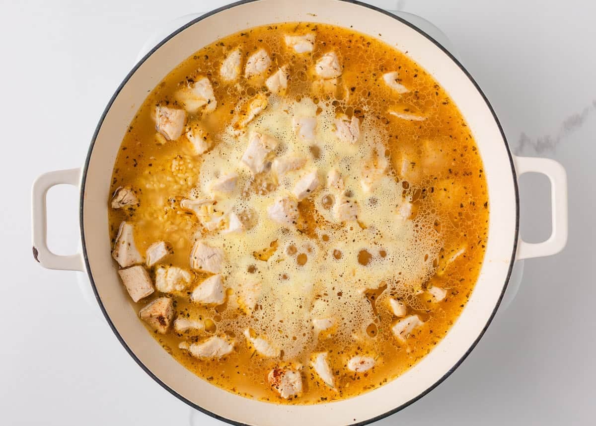 Chicken and orzo simmering in chicken broth with seasonings in a large skillet.