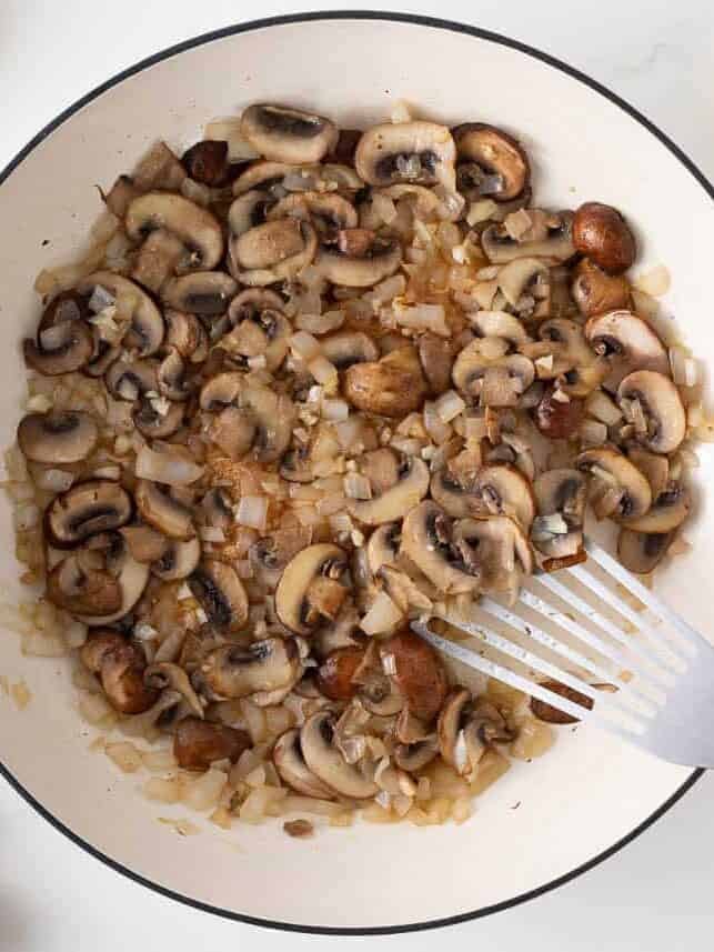 Mushrooms and onions sautéing in a skillet until softened and lightly browned.